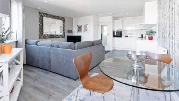 Ein modernes Wohnzimmer mit einem grauen Sofa, einem runden Glastisch und einem Holzstuhl.