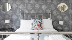 Ein ordentlich bezogenes Bett mit weißen Leinen, einem floralen Kopfkissen und zwei Nachttischlampen auf einem Nachttisch.