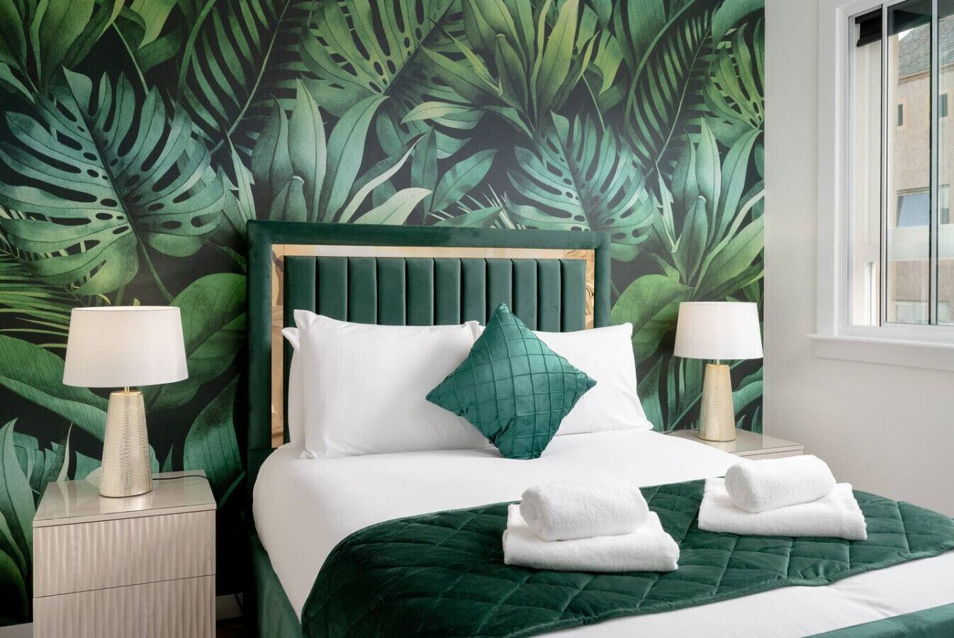 A bedroom with a green leaf-patterned wallpaper, a wooden headboard, white bedding, and two bedside lamps.