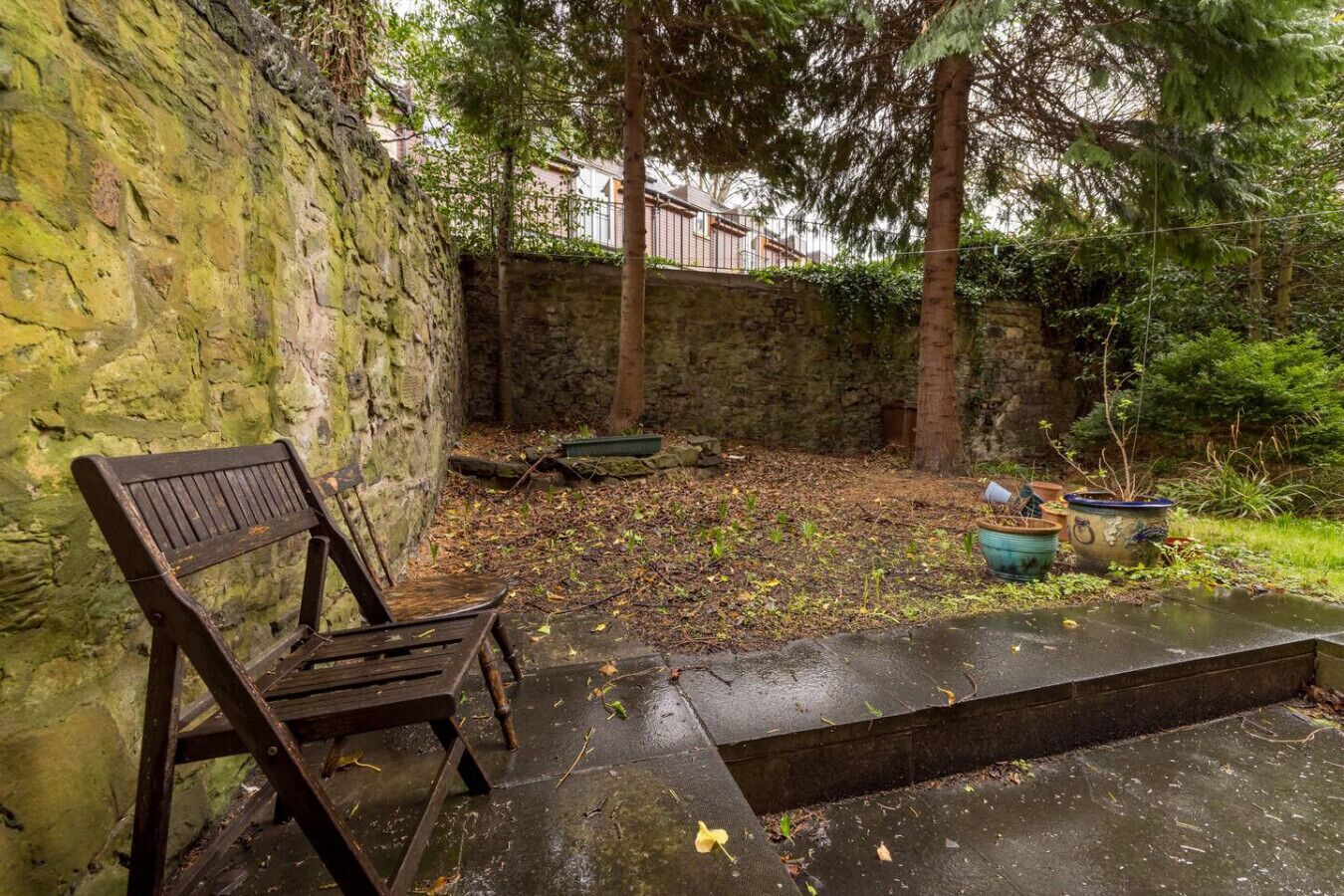 A stone wall, a wooden bench, and a small garden area with potted plants.