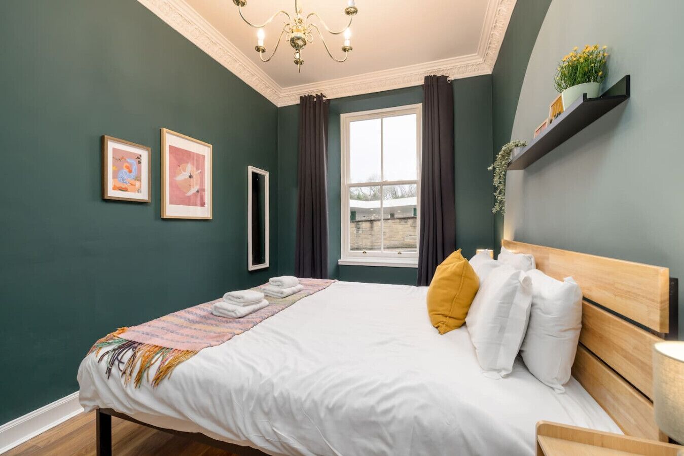Une chambre à coucher avec un lit, une fenêtre, un lustre et une étagère avec des plantes.