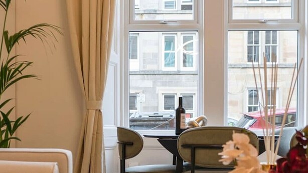 Ett vardagsrum med en soffa, ett matbord med stolar, en krukväxt och en vas med blommor.