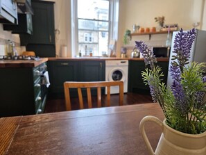 A kitchen with dark cabinets, a wooden chair, a washing machine, and a vase with purple flowers on the counter. - Montgomery Mews in Leith (Edinburgh)