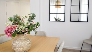 Un coin repas avec une table en bois, un vase en osier contenant des fleurs et deux miroirs fixés au mur.