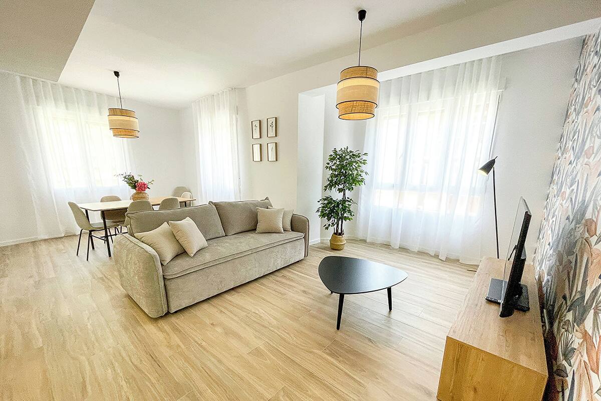 Ein modernes Wohnzimmer mit einer Couch, einem Esstisch und Stühlen. Eine Topfpflanze und eine Stehlampe sind ebenfalls vorhanden.
