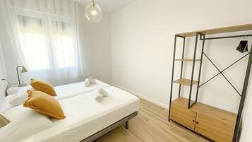 A bedroom with a bed, two pillows, a bedside table, a lamp, a wardrobe, and a hanging light fixture.