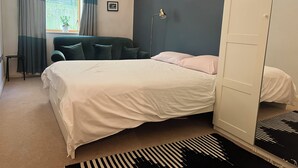 Ein Schlafzimmer mit Bett, Stuhl, Schreibtisch, Lampe, Kleiderschrank und einem Fenster mit Vorhängen.