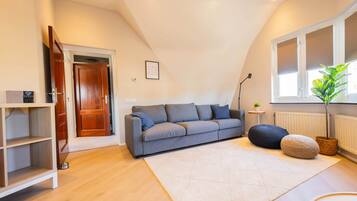 A modern living room with a grey sofa, a white rug, wooden flooring, and a window with blinds.