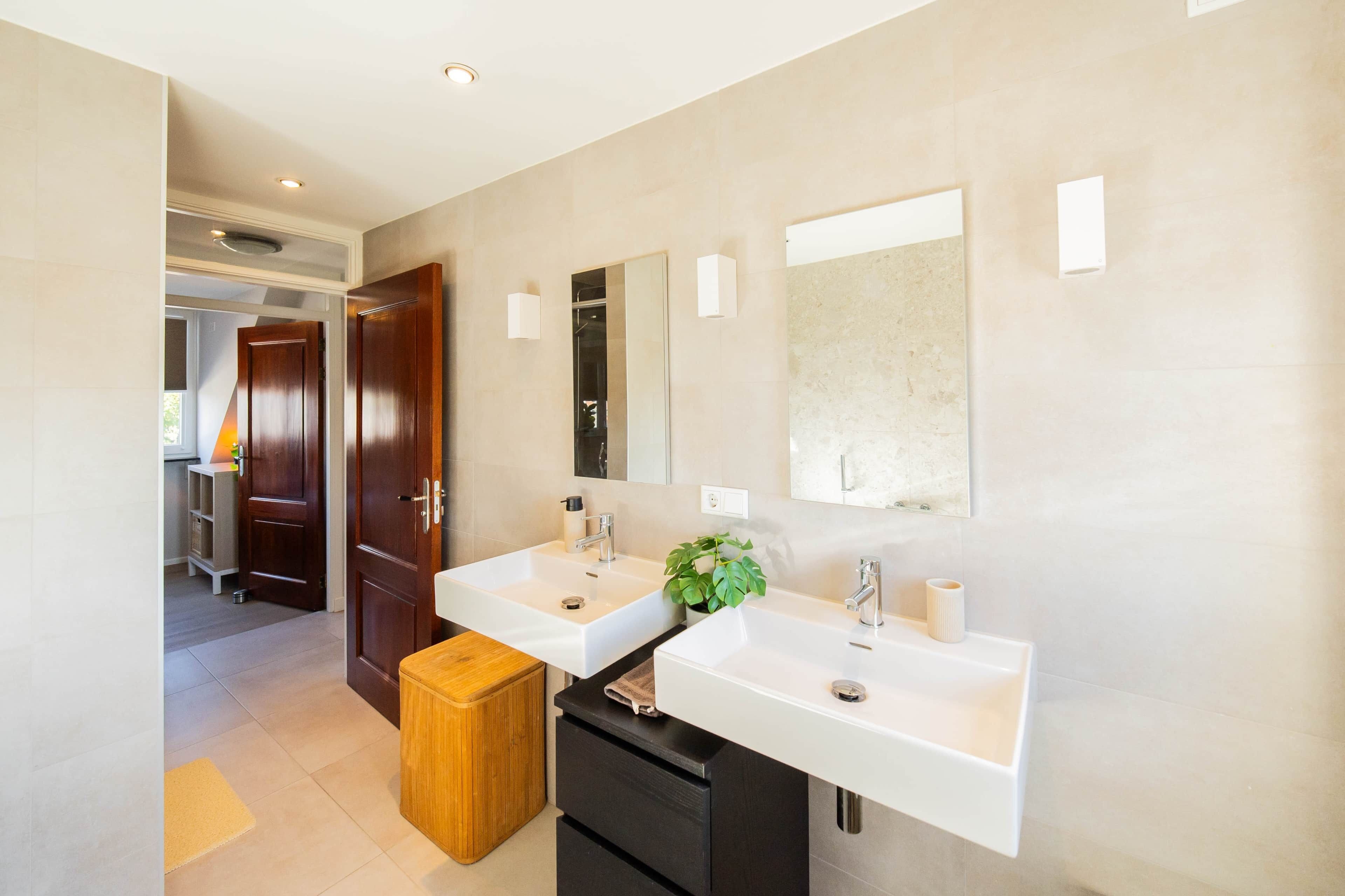 A modern bathroom with two sinks, a wooden bench, and a large mirror.
