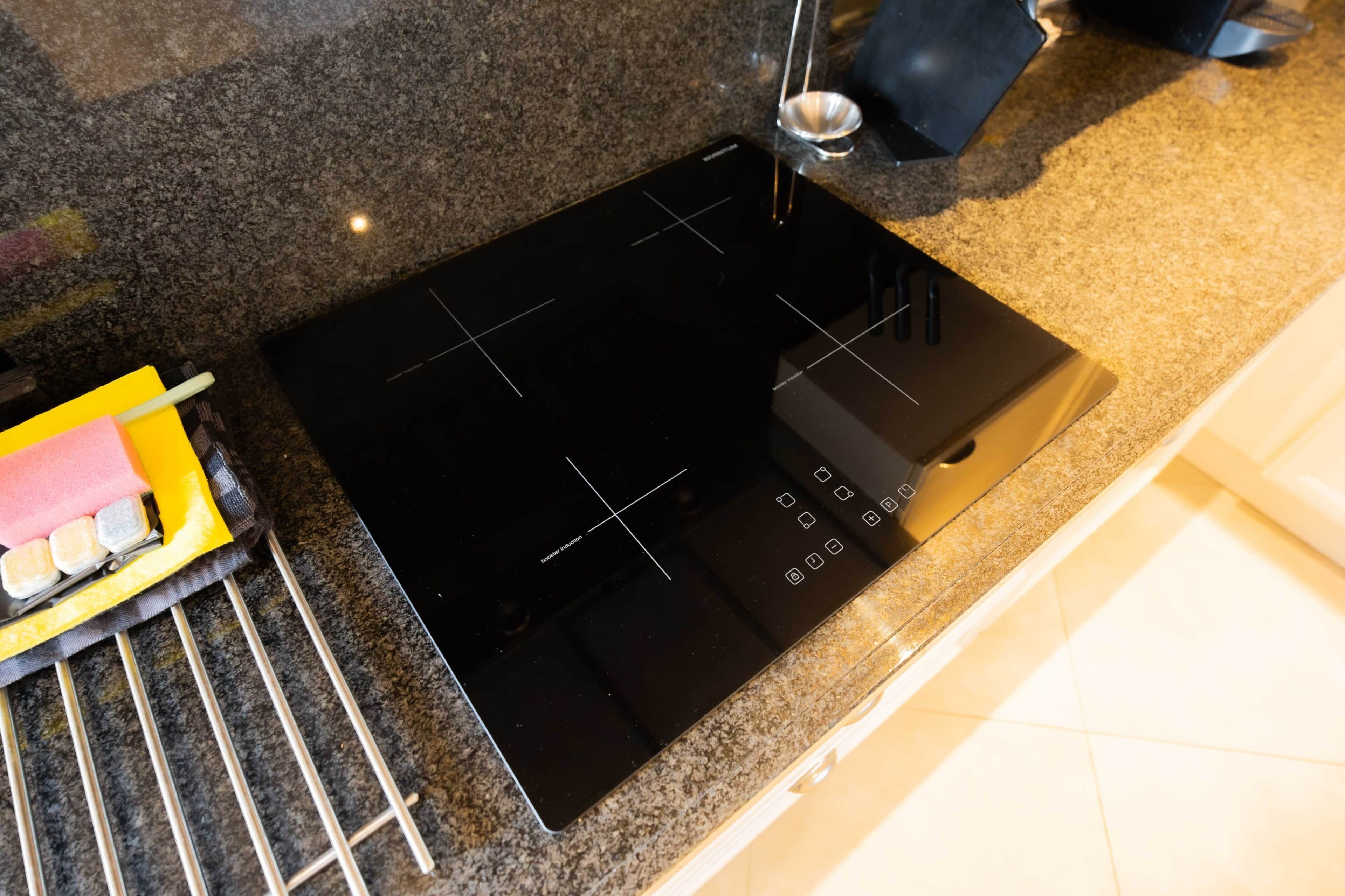 A kitchen with a black induction cooktop, a stainless steel sink, and a yellow cleaning tool.