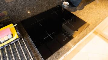 A kitchen with a black induction cooktop, a stainless steel sink, and a yellow cleaning tool.