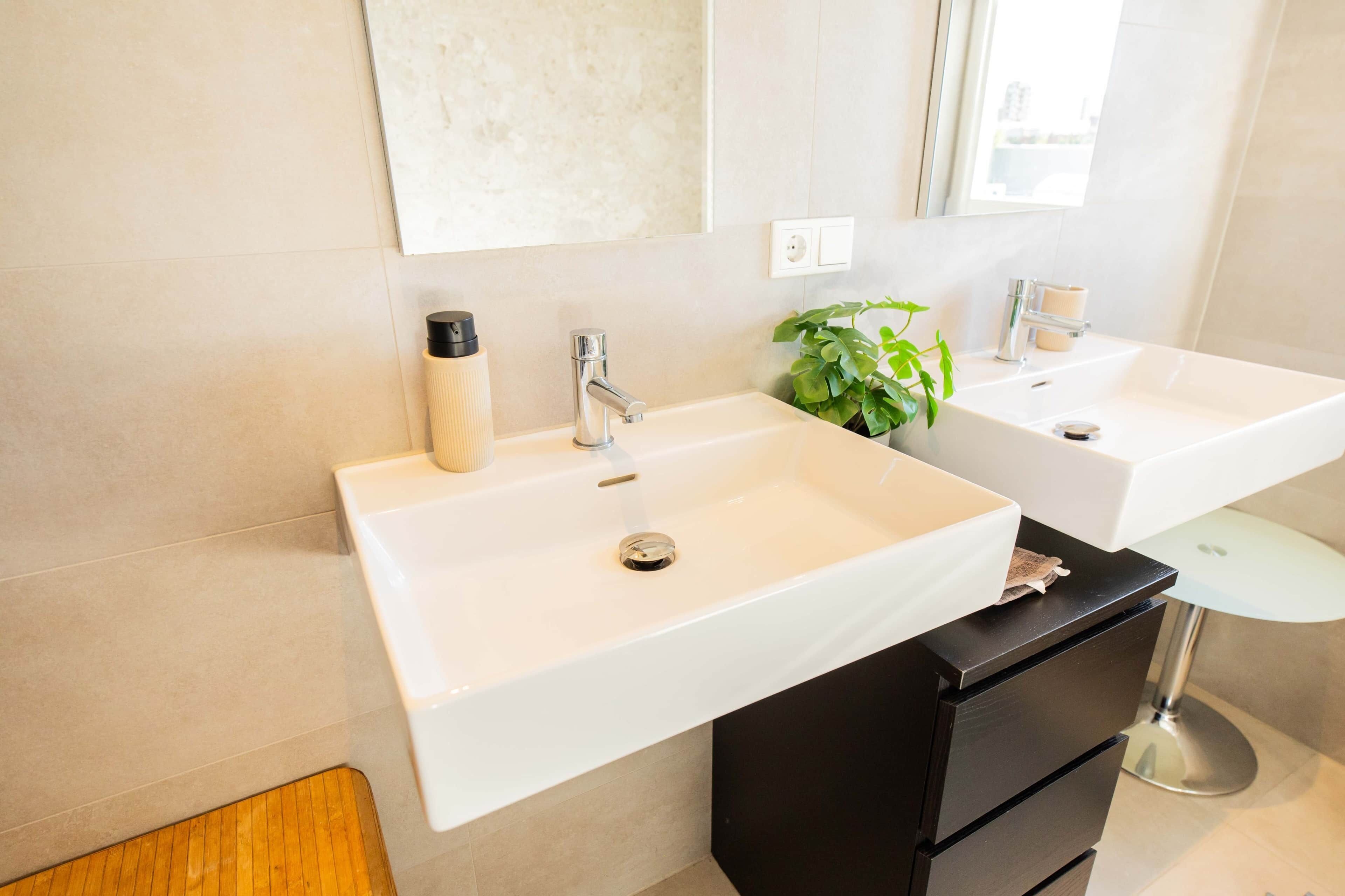 Un baño moderno con dos lavamanos blancos, un mueble de tocador negro y un espejo redondo pequeño.