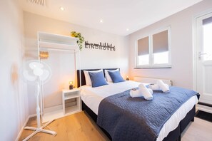 Una camera d'albergo con un letto, comodini, una ventola a parete e una finestra con persiane.