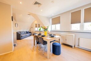 Un comedor moderno con una mesa dispuesta para cuatro personas, un sofá y un amplio ventanal con persianas.