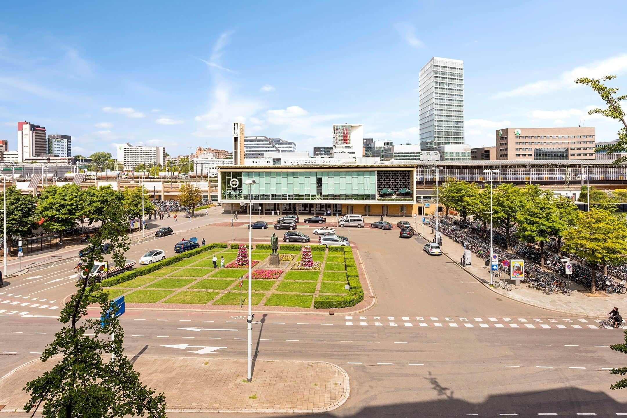 Een modern gebouw met een binnentuin, omgeven door een parkeerplaats en een weg met verkeer.