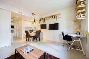En moderne opholdsstue med spiseplads, arbejdsområde og et TV ophængt på væggen.