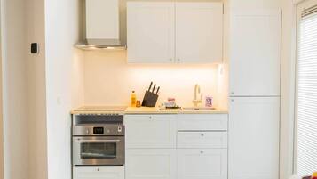 A compact kitchen with white cabinets, a stainless steel oven, a built-in microwave, and a small countertop with a knife block and a few items.