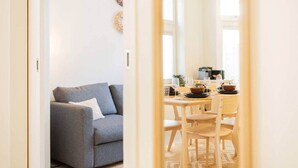 Un coin repas avec une table dressée pour quatre personnes, un canapé gris et une fenêtre laissant entrer la lumière naturelle.