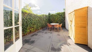 Un patio con una mesa y sillas, un armario de madera y una pared de ladrillo blanco.