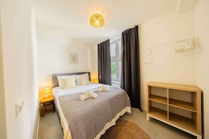 Une chambre à coucher avec un lit, des lampes de chevet, une table de chevet, une fenêtre avec des rideaux et une étagère en bois.