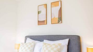 Habitación de hotel con cabecera gris, dos mesitas de noche con lámparas y dos cuadros abstractos en la pared.