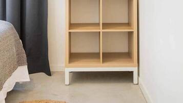 Een slaapkamer met een bed, een donker gordijn, een witte muur, een houten wandplank en een witte hanglamp.