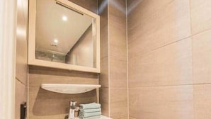 Une salle de bain moderne avec un lavabo blanc, un meuble-lavabo en bois, un miroir et un mur recouvert de carreaux.