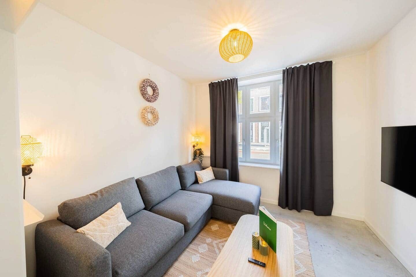 Een moderne woonkamer met een grijze modulaire bank, een flatscreen televisie aan de muur en een kleine houten salontafel.