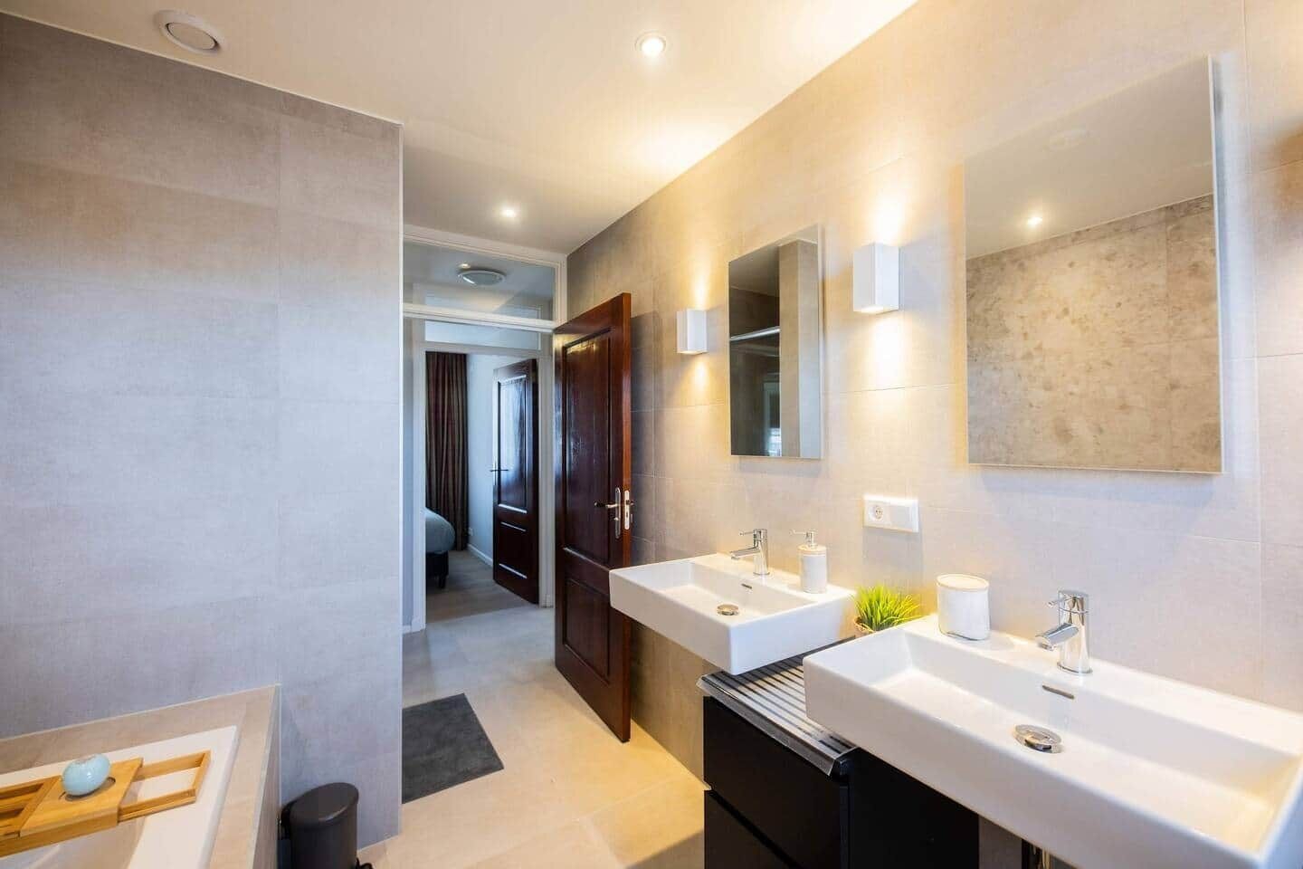 Een moderne badkamer met twee wasbakken, een spiegel en een douche.