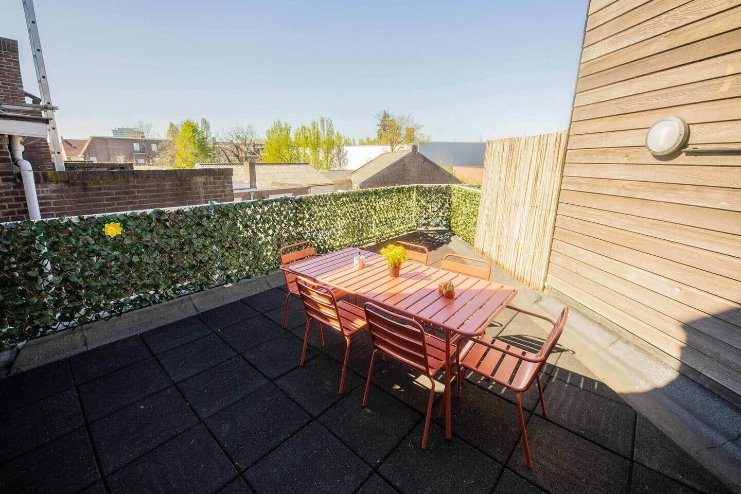 A patio with a wooden table and chairs, a potted plant, and a wall-mounted light fixture.