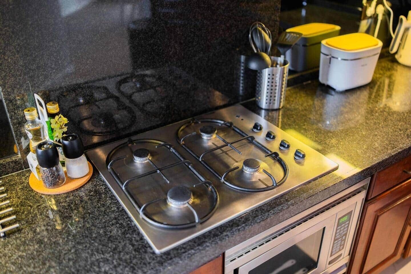 A kitchen with a stainless steel stove, a microwave, and a coffee maker. There are salt and pepper shakers, a knife block, and a small plant on the counter.
