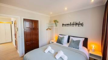 A hotel room with a bed, a wardrobe, a wardrobe mirror, a shelf with a plant, and a wall with the text "EINDHOVEN".