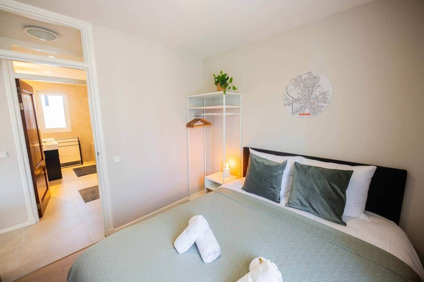 Un dormitorio con una cama, una mesita de noche con lámpara, una planta colgante y un reloj de pared.
