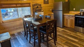 Una cocina acogedora estilo cabaña con paredes de madera, una mesa de comedor con sillas, un refrigerador y una estufa.