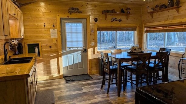 Interior acogedor de una cabaña con cocina, comedor y un amplio ventanal con vistas a un bosque.