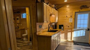Interior de una cabaña de madera con zona de cocina que incluye un lavamanos, armarios y una ventana.