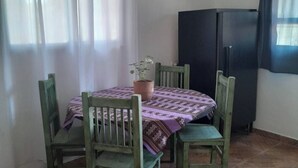 Un coin repas avec une table dressée pour quatre personnes, entouré de chaises vertes, d’une plante en pot et d’un réfrigérateur noir.