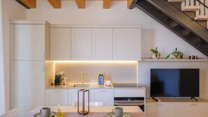 Een moderne keuken met witte kasten, een eettafel met twee stoelen, een televisie en een trap.