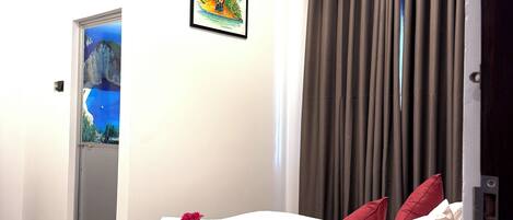 A hotel room with a bed, a remote control, a picture on the wall, and a door leading to another room.
