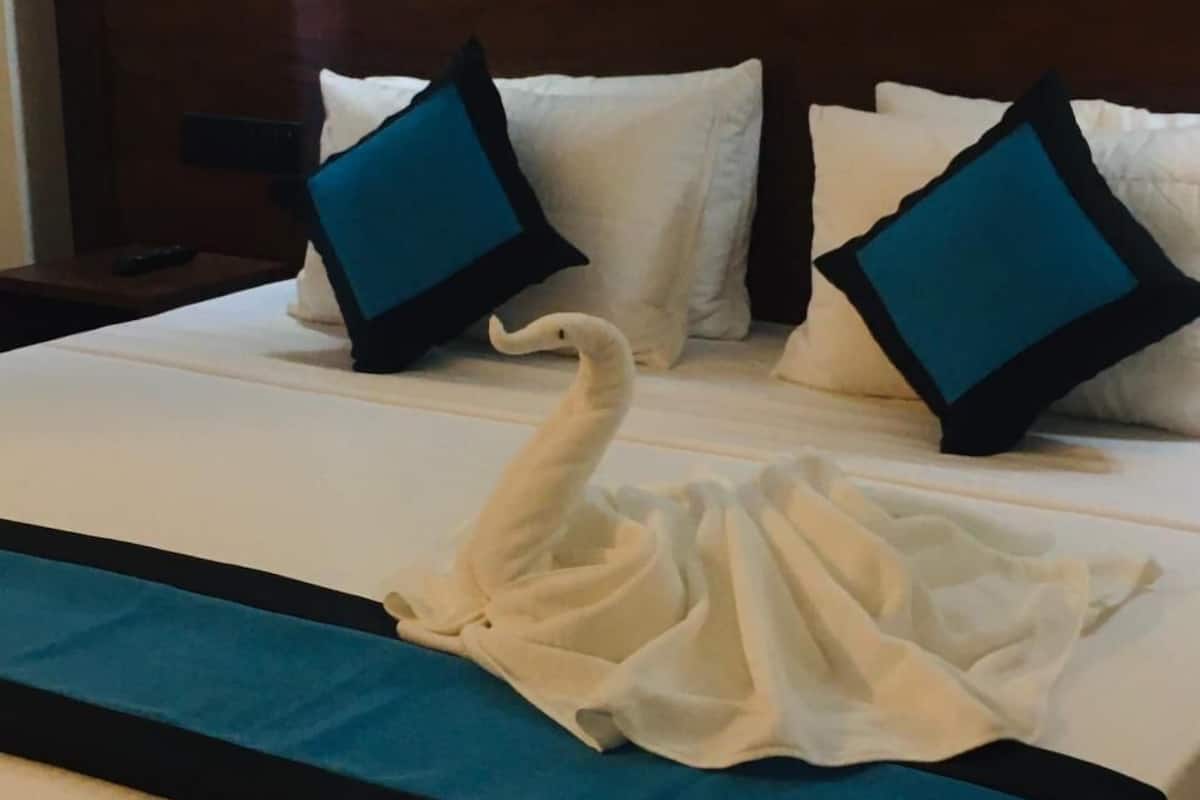 Une chambre d’hôtel avec un lit parfaitement fait, une couvre-lit bleue et blanche, et une serviette pliée en forme de cygne.