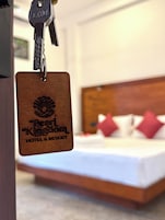 A keychain with "Pearl Kingdom Hotel & Resort" engraved on it, hanging in front of a bed with a wooden headboard and red pillows.