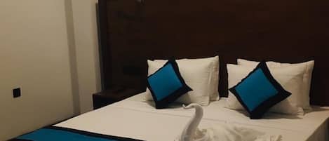 A hotel room with a large bed, white bedding, and blue pillows.
