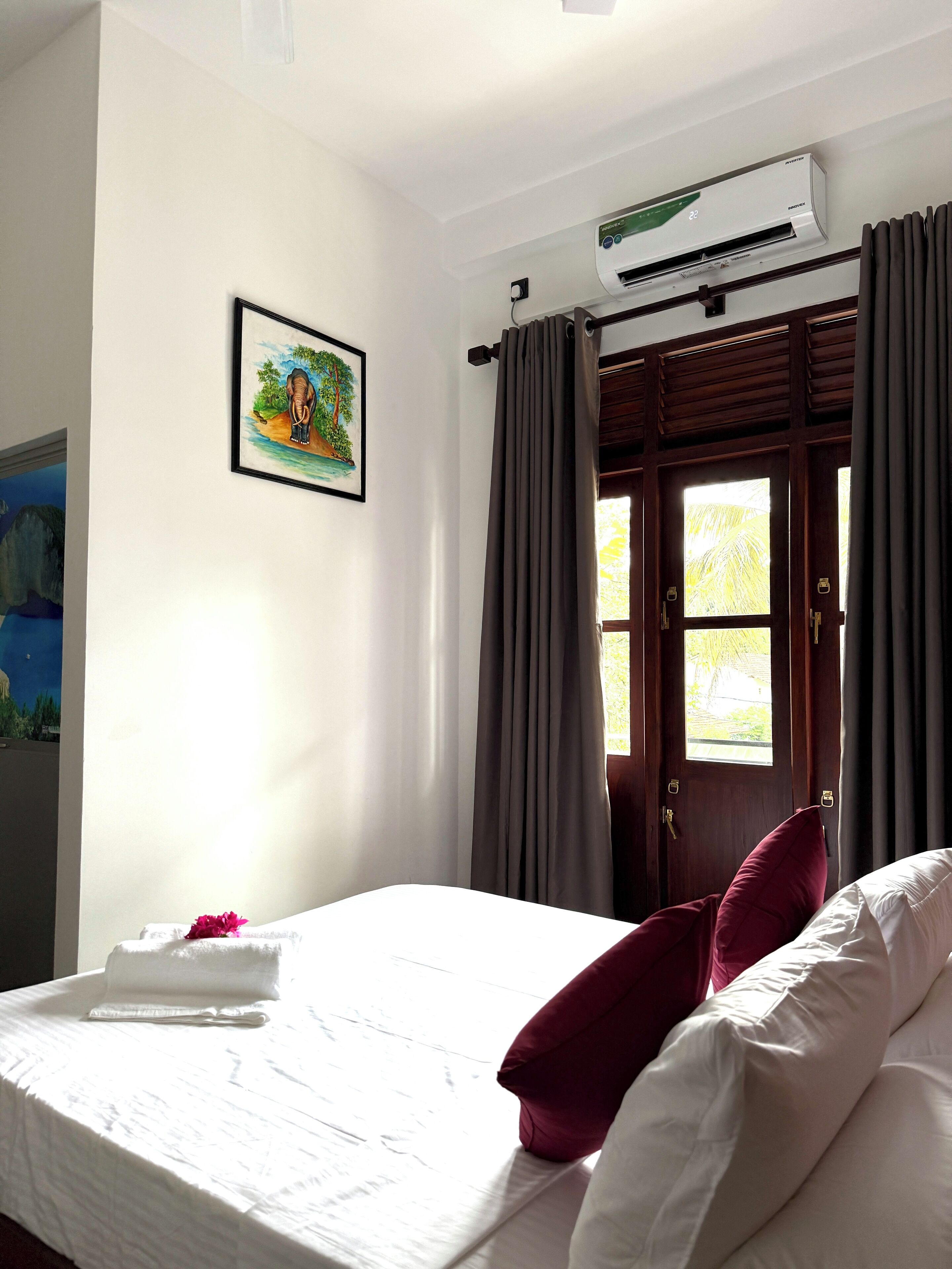 Habitación de hotel con cama, un cuadro, unidad de aire acondicionado y vista a través de una puerta.