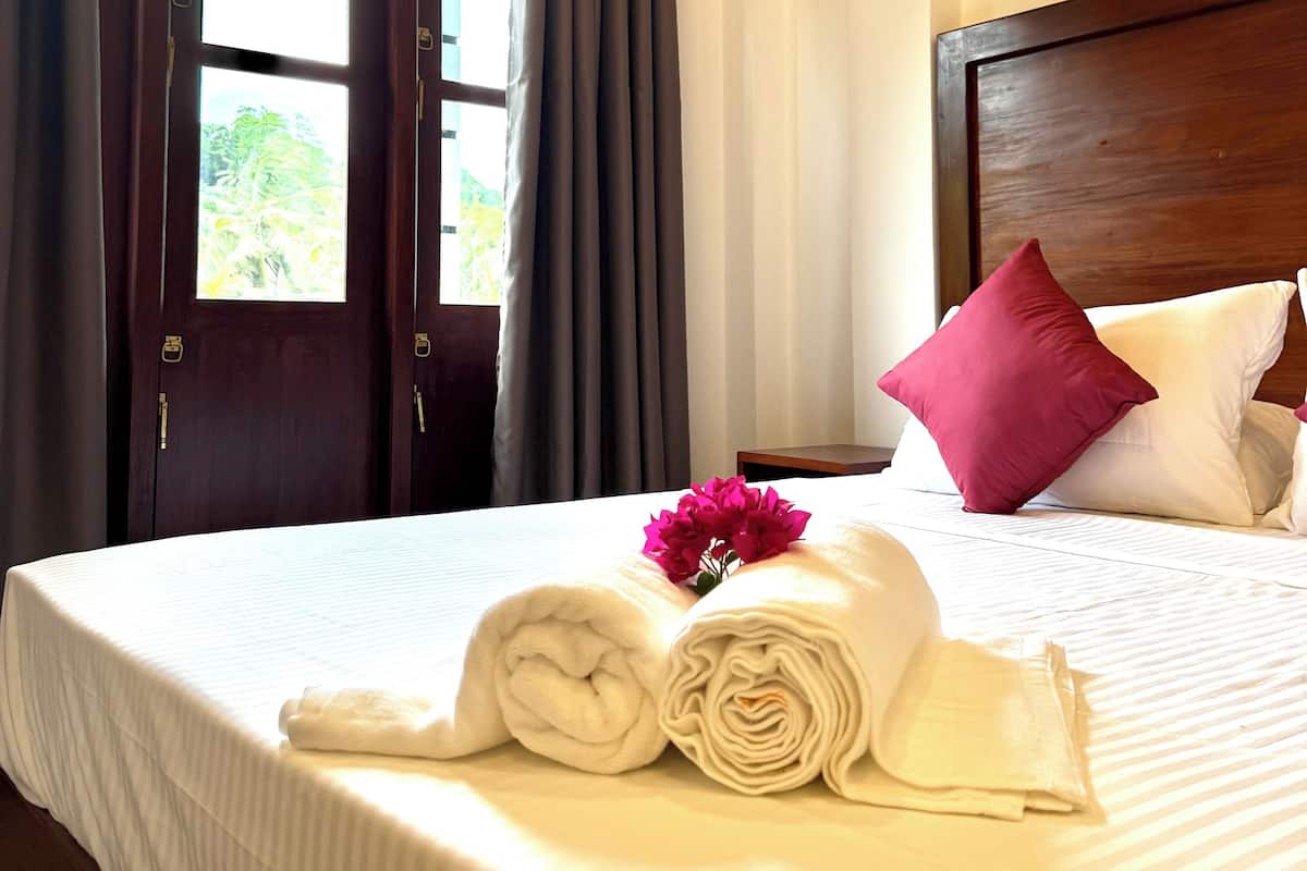 Une chambre d’hôtel avec un lit, une fenêtre avec des rideaux et une vue sur la verdure.