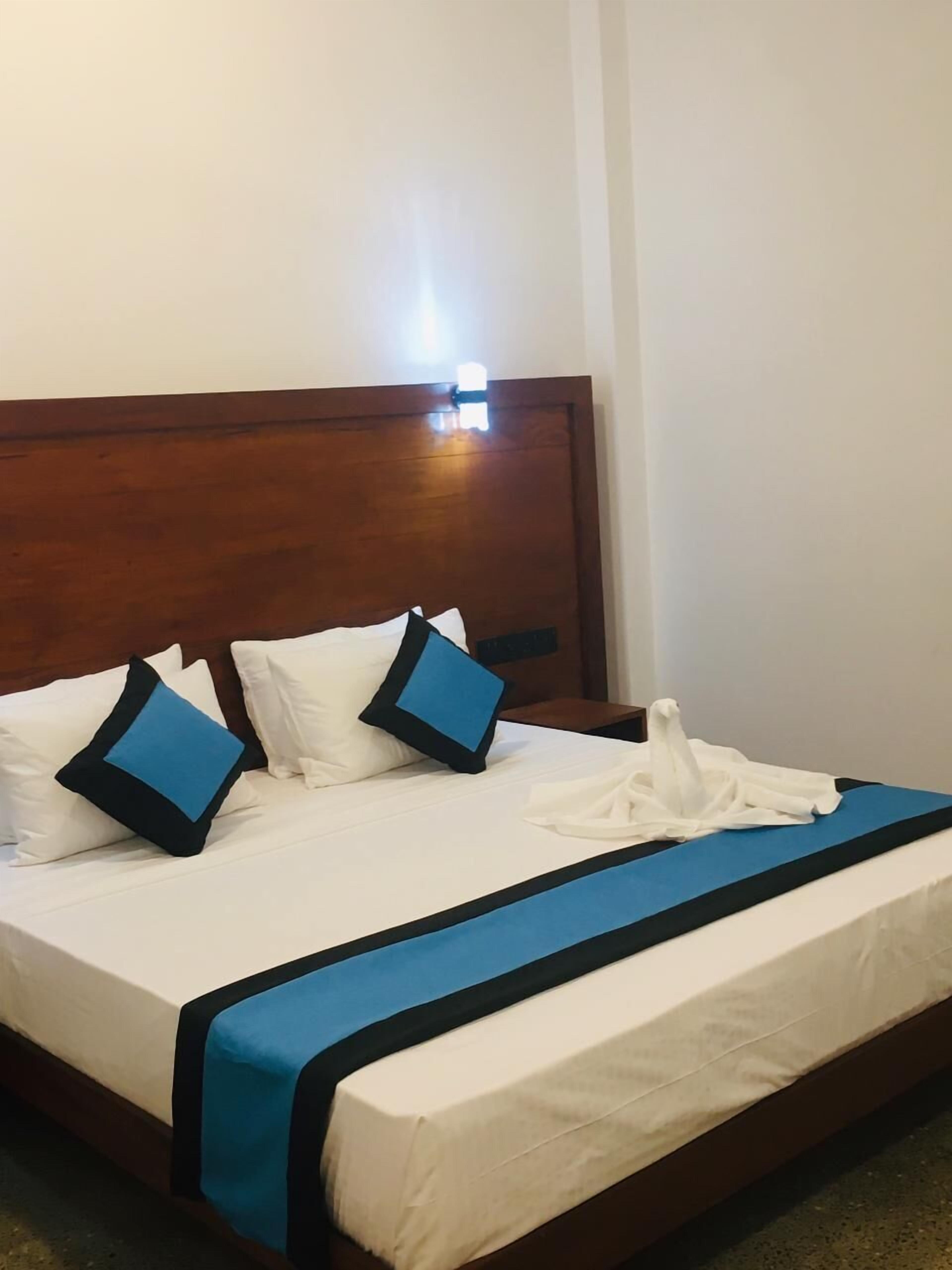 A hotel room with a wooden headboard, a white bedspread, and blue accents on the pillows and bed skirt.