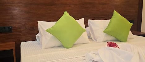 A hotel room with a wooden headboard, a bed with white bedding, green pillows, and a blue accent on the bed.