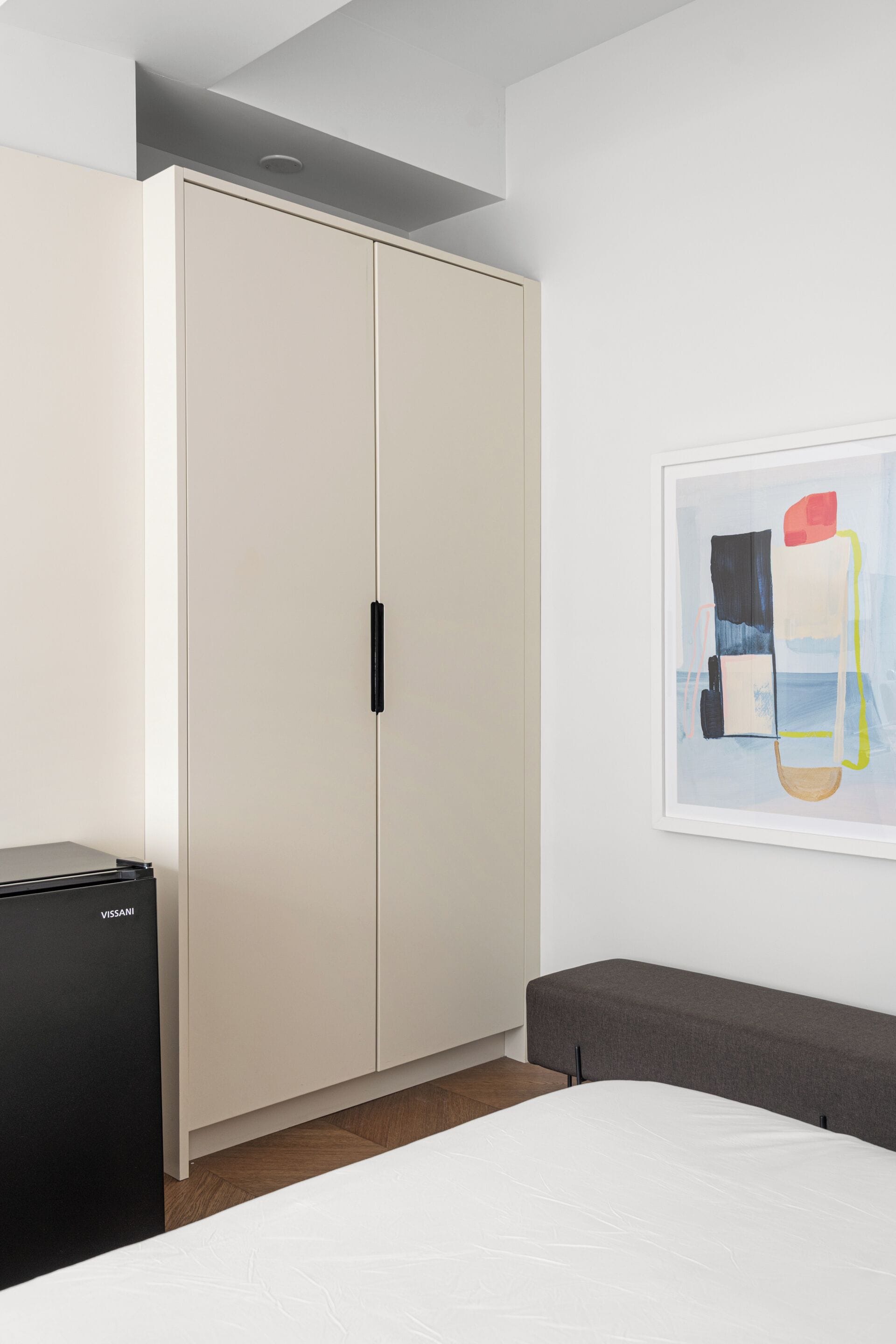 A bedroom with a bed, a wardrobe, and a painting on the wall.