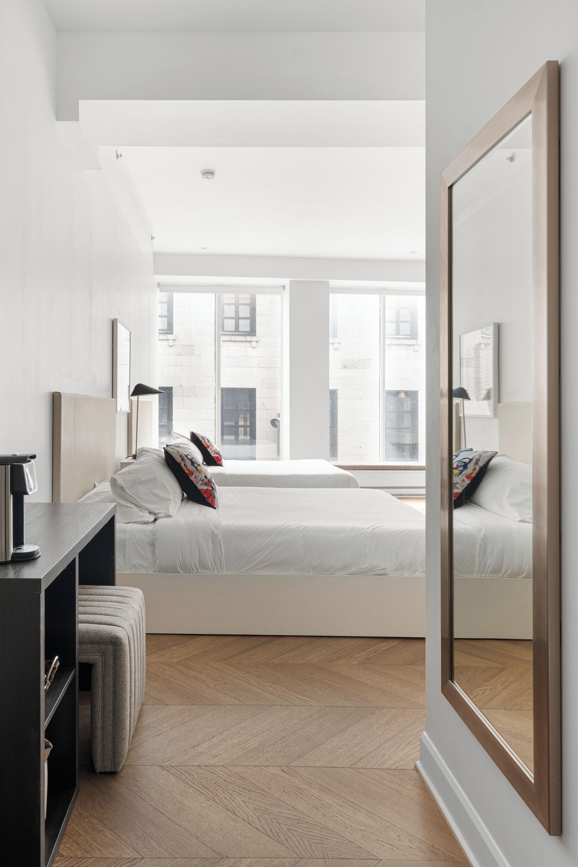 A modern hotel room with a large bed, a bedside table, a wardrobe, and a large mirror.
