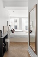 A modern hotel room with a large bed, a bedside table, a wardrobe, and a large mirror.