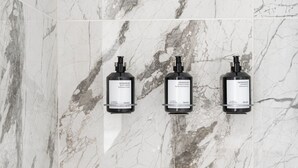 A bathroom with marble tiles and three black dispensers labeled "HERBALISMR" for shampoo and conditioner. - The Bowery Lofts Hotel (Montréal)